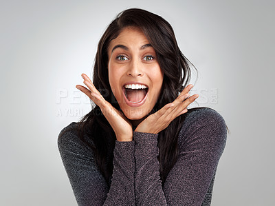 Buy stock photo Shot of a young woman looking surprised while standing against a grey background