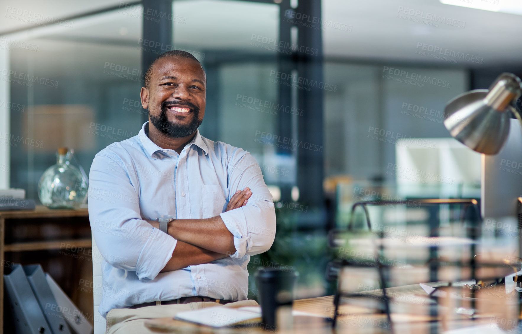 Buy stock photo Cropped portrait of a handsome mature businessman sitting alone in his office at night with his arms folded