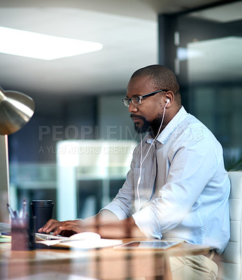 Buy stock photo Cropped shot of a mature businessman sitting in his office at night and using his computer while wearing earphones