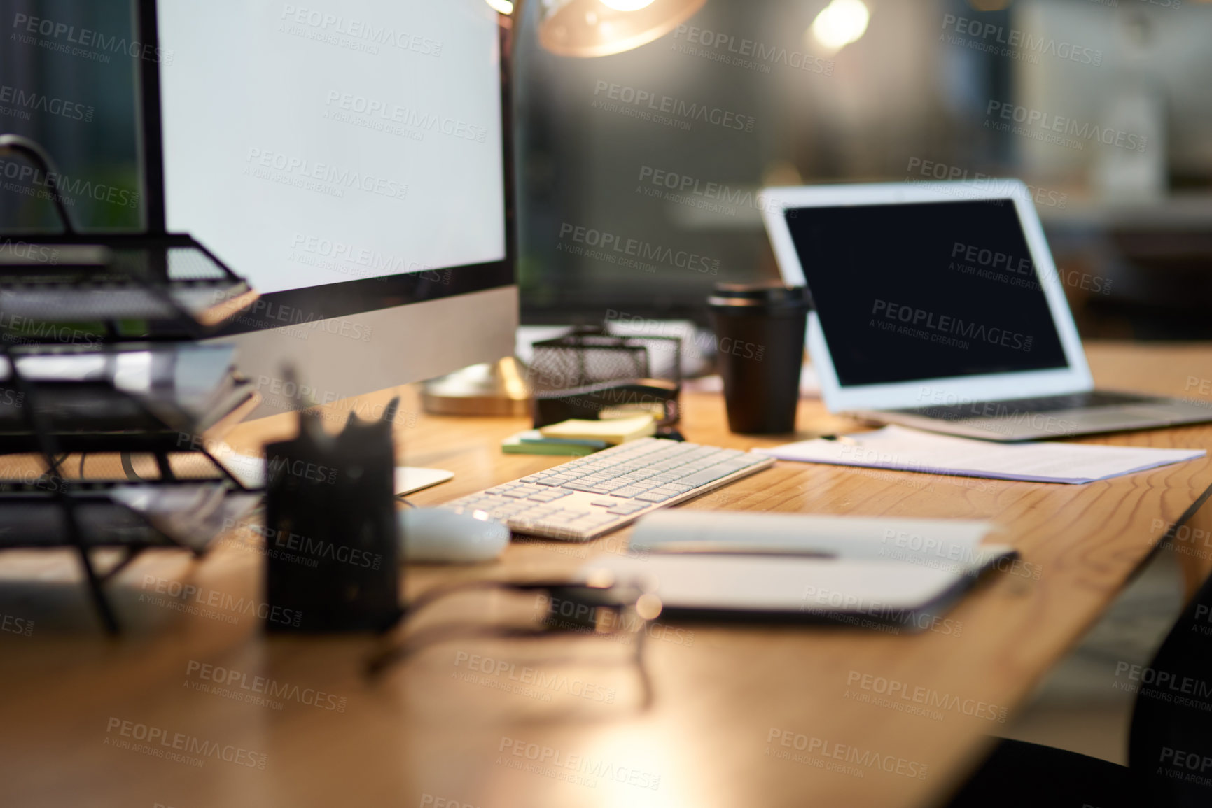 Buy stock photo Cropped shot of an office workstation scattered with stationery and technology during the late hours of the evening