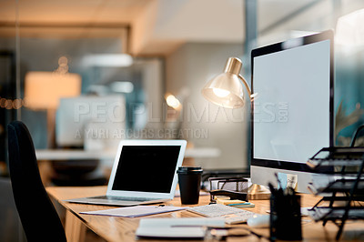 Buy stock photo Cropped shot of an office workstation scattered with stationery and technology during the late hours of the evening