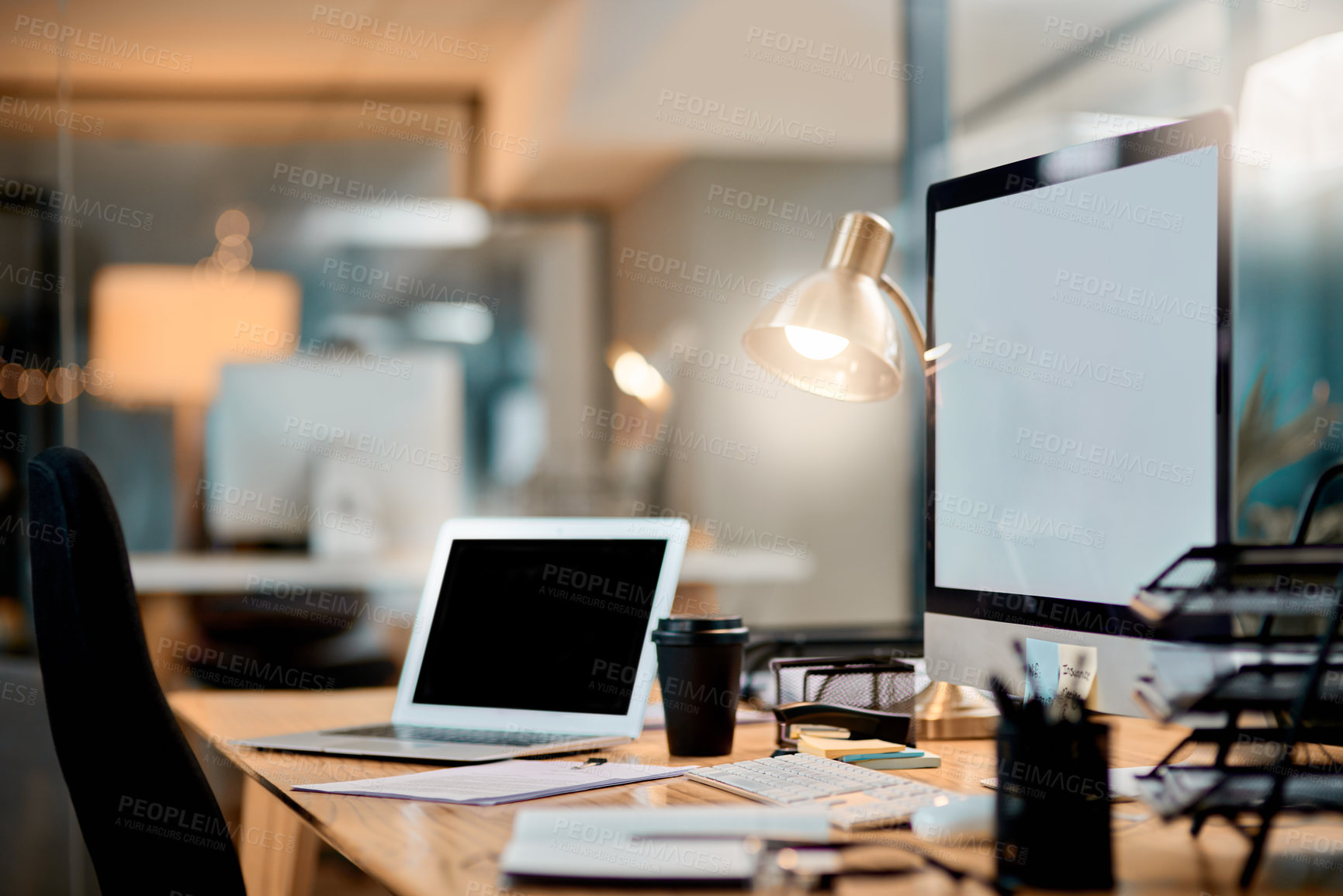 Buy stock photo Cropped shot of an office workstation scattered with stationery and technology during the late hours of the evening