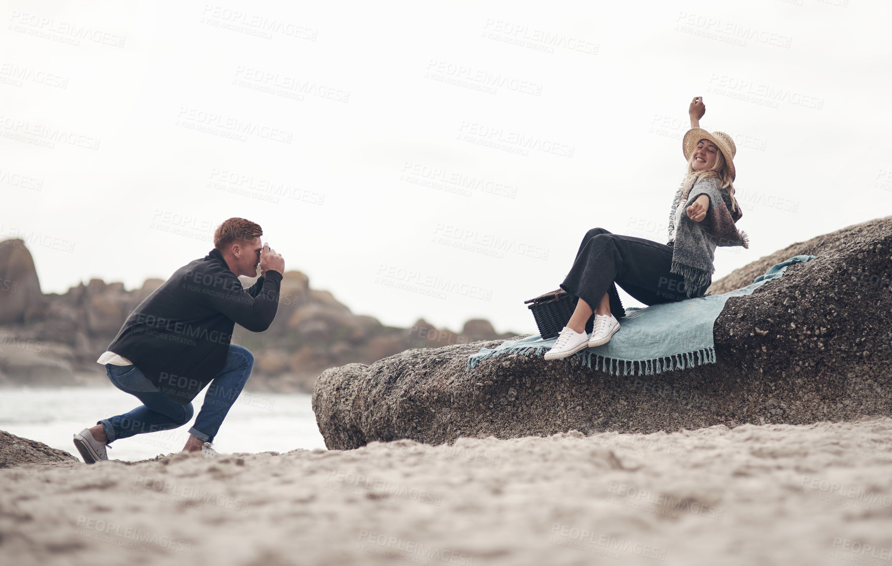 Buy stock photo Woman, man and photo for picnic at beach with smile, bonding or camera for memory on vacation. People, couple and photography in relationship, happy and space on rock with love for seaside holiday