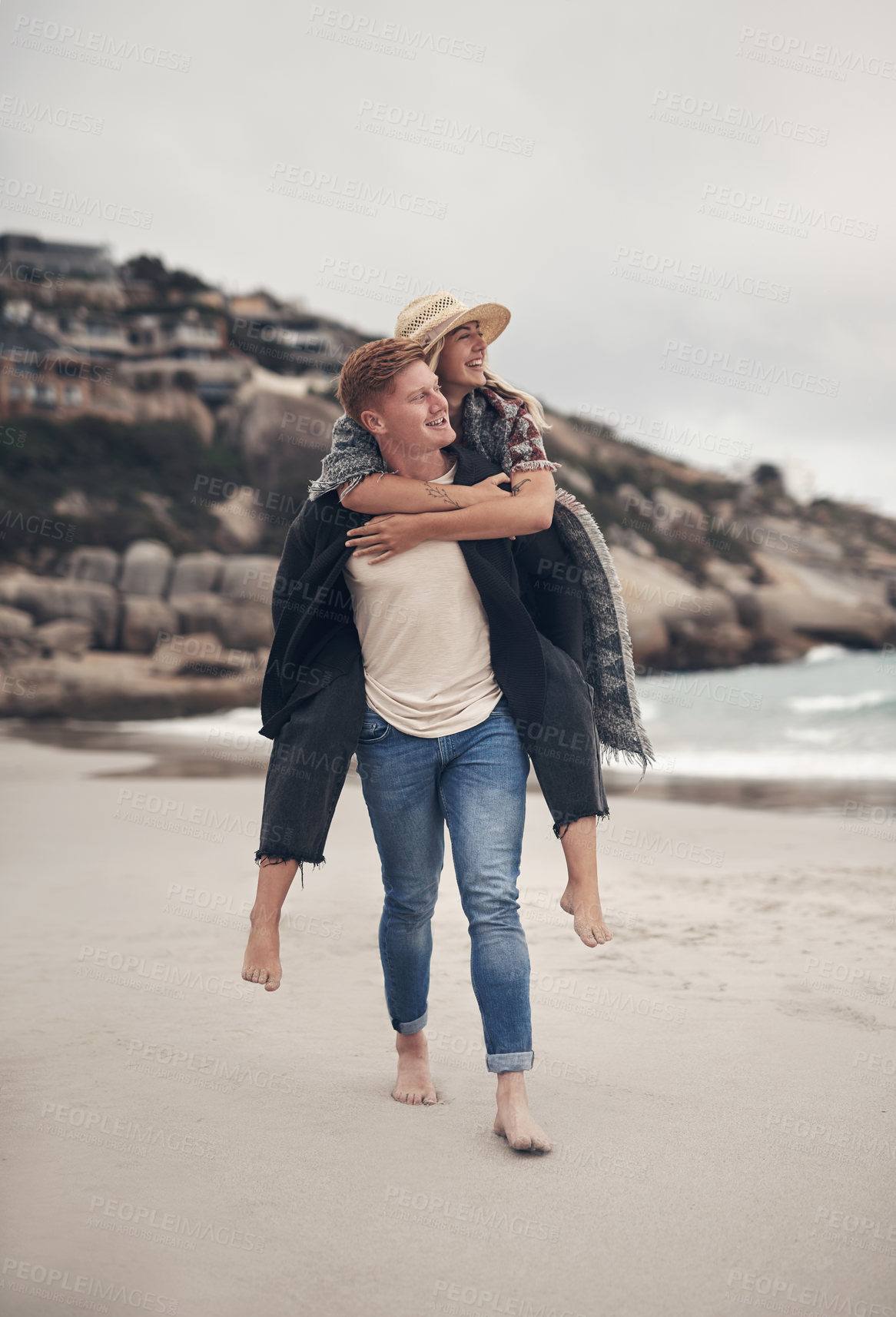 Buy stock photo Shot of a man piggybacking his girlfriend while walking on the beach