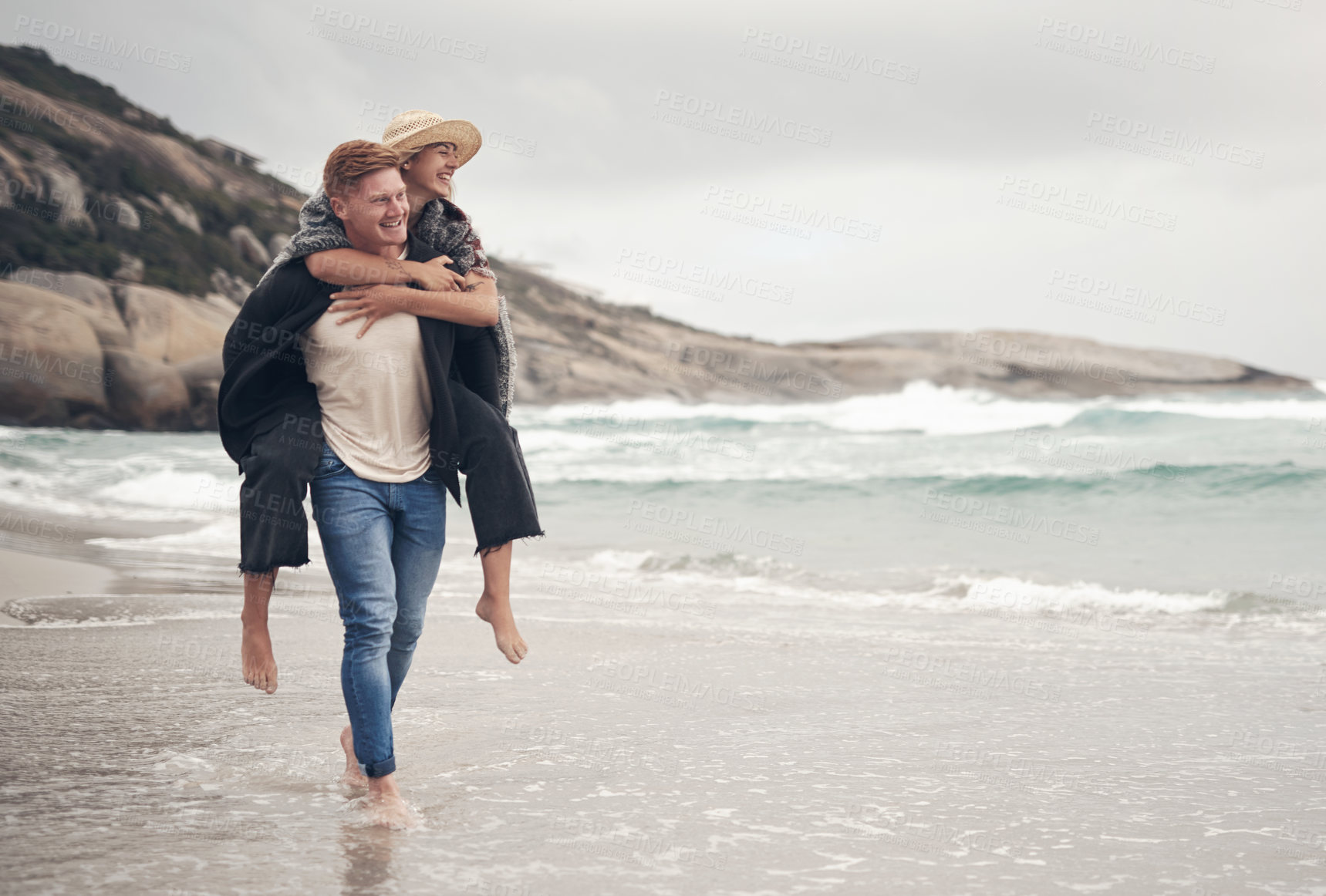 Buy stock photo Shot of a man piggybacking his girlfriend while walking on the beach