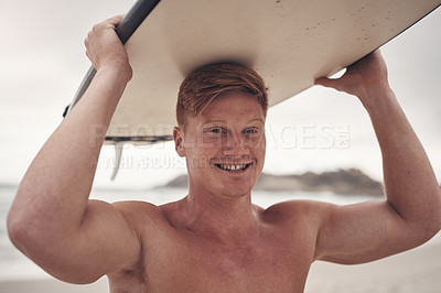 Buy stock photo Shot of a young man carrying his surfboard on his head while at the beach