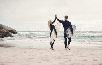 Buy stock photo Shot of a couple giving each other a high five while out at the beach with their surfboards