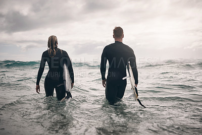Buy stock photo Shot of a young couple going out into ocean with their surfboards