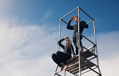 Buy stock photo Shot of two people wearing wetsuits while sitting on a lifeguard tower