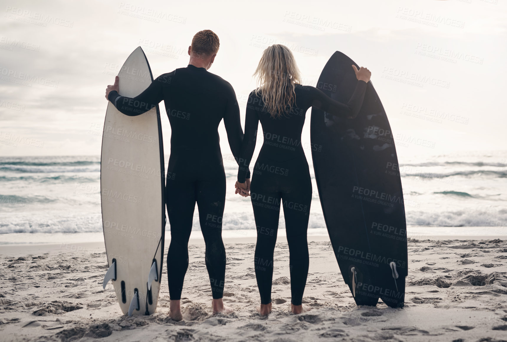 Buy stock photo Shot of a young couple standing on the beach with their surfboards