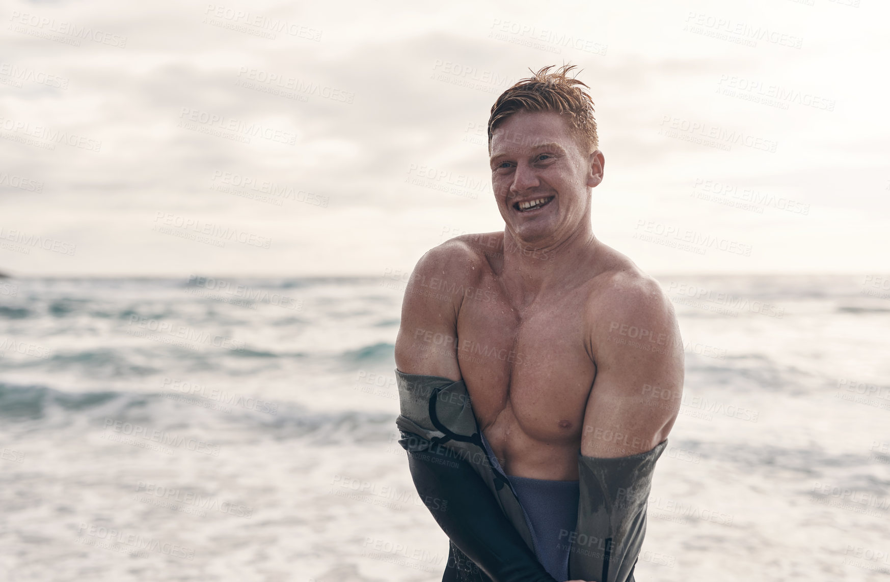 Buy stock photo Cropped shot of a young man taking off his wetsuit