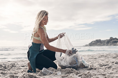 Buy stock photo Shot of a woman holding a plastic bag while picking up trash on the beach