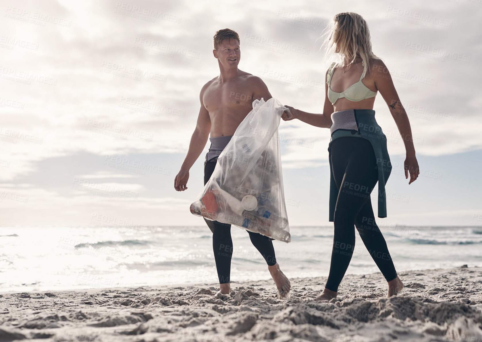 Buy stock photo Shot of a young couple doing a beach clean while wearing wetsuits