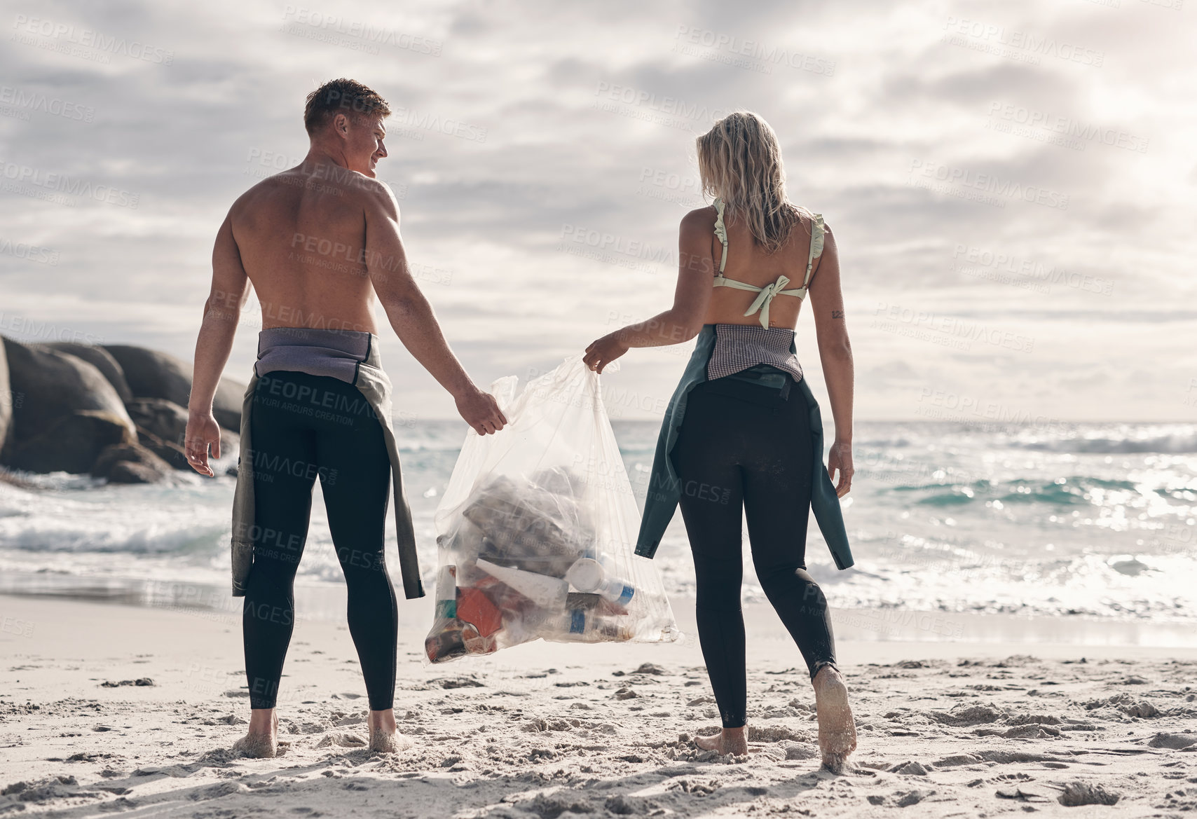 Buy stock photo Shot of a young couple doing a beach clean while wearing wetsuits