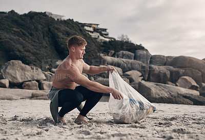 Buy stock photo Shot of a man holding a plastic bag while picking up trash on the beach