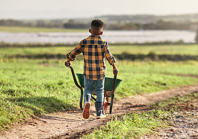 Buy stock photo Rearview shot of a young boy pushing a wheelbarrow on a farm