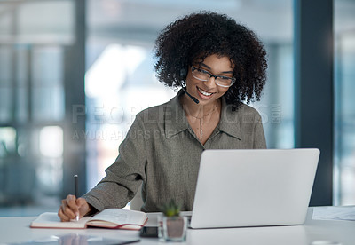 Buy stock photo Shot of a young female agent smiling while making notes working in a call centre