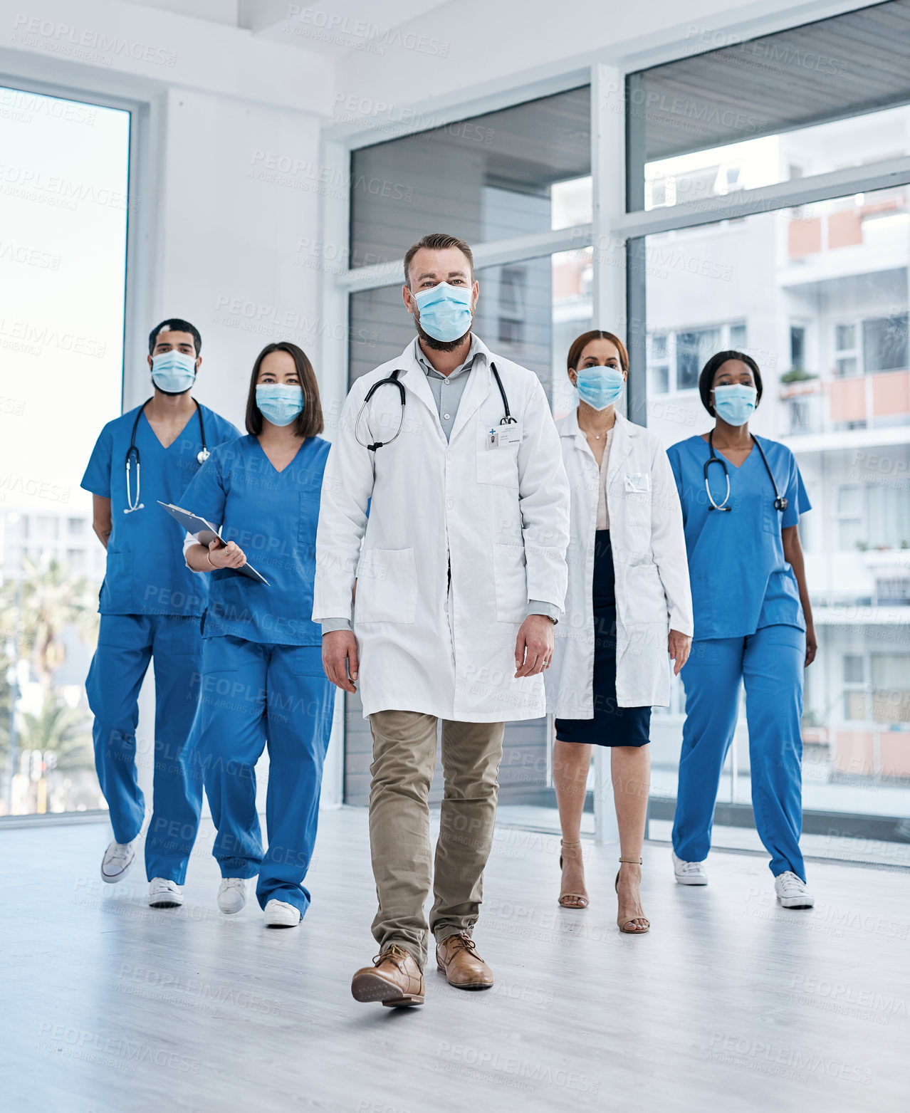 Buy stock photo Shot of a group of medical practitioners wearing face masks while walking in a hospital