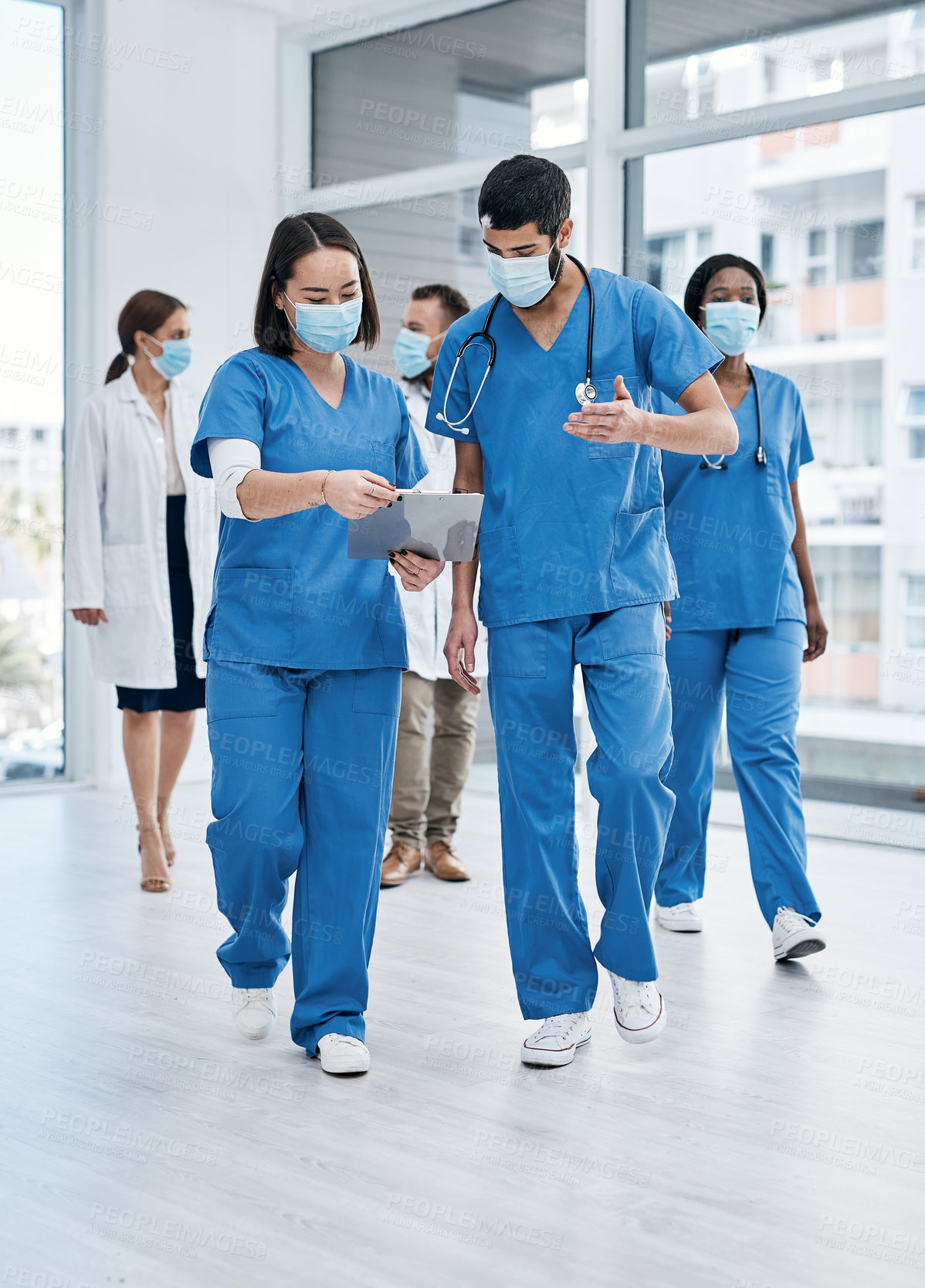 Buy stock photo Shot of two medical practitioners going through notes while walking in a busy hospital