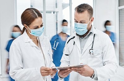 Buy stock photo Shot of two doctors going through notes in a busy hospital