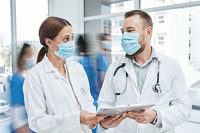 Buy stock photo Shot of two doctors going through notes in a busy hospital