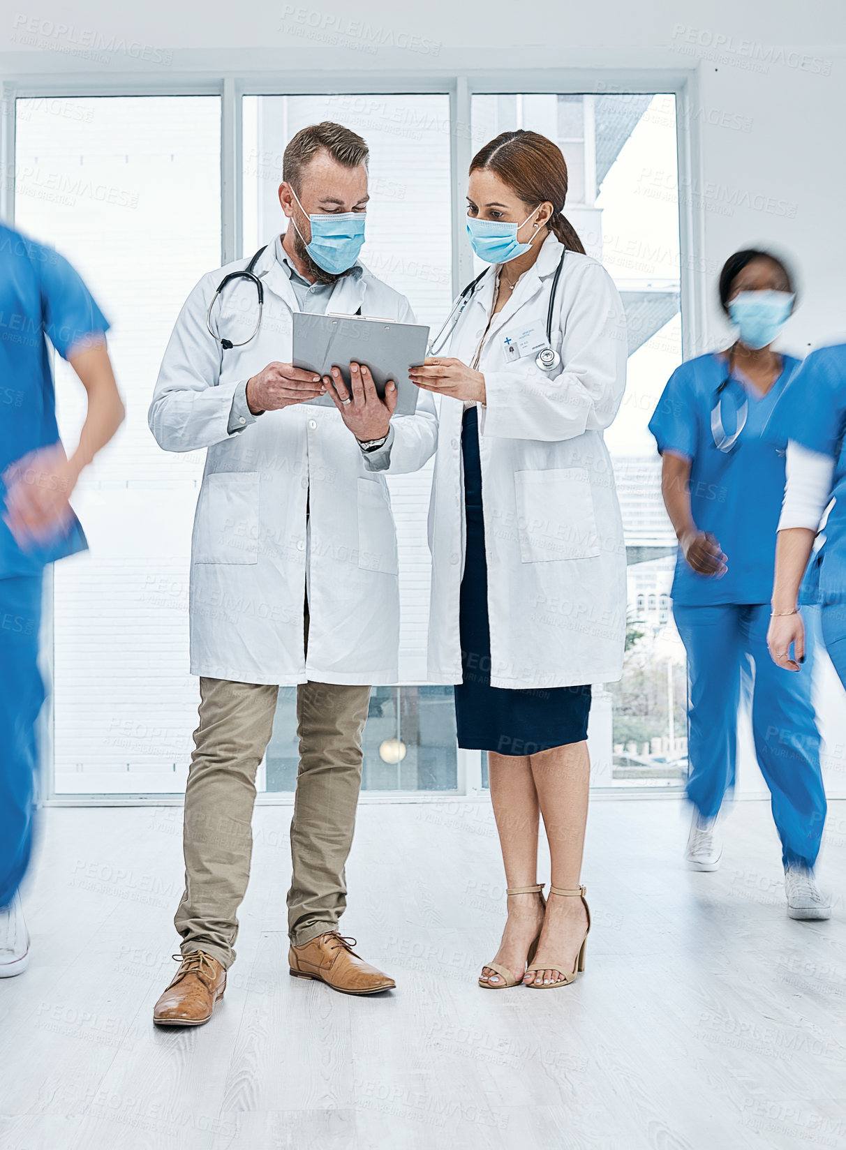 Buy stock photo Shot of two doctors going through notes in a busy hospital