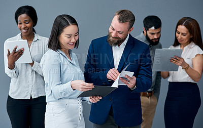 Buy stock photo Shot of two businesspeople going through paperwork while their colleagues are working in the background