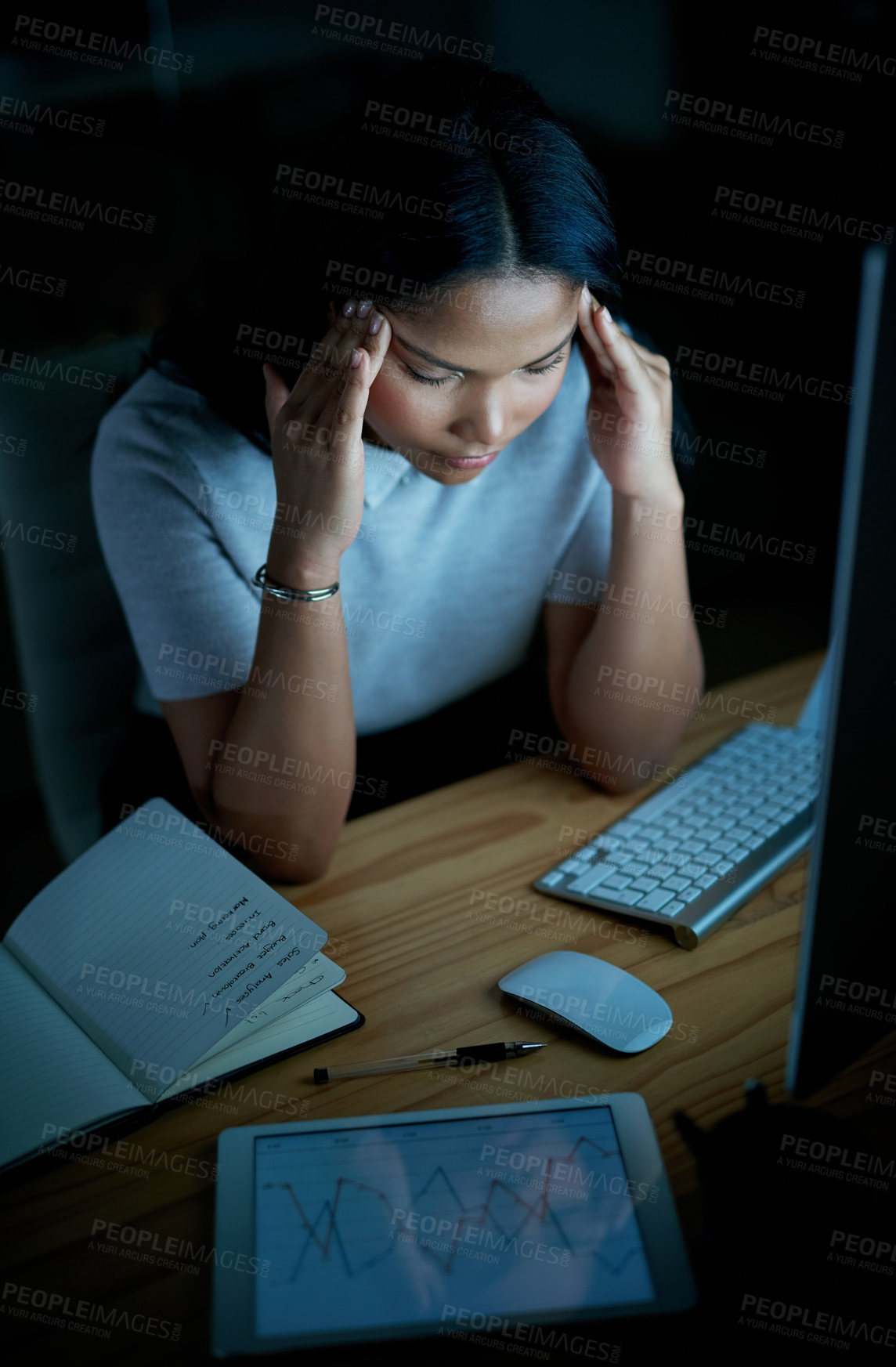 Buy stock photo Shot of a young businesswoman looking stressed while using a computer during a late night at work