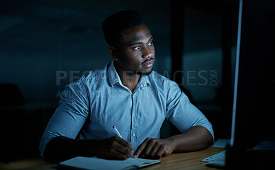 Buy stock photo Shot of a young businessman writing in a notebook and using a computer during a late night at work