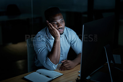 Buy stock photo Shot of a young businessman looking bored while using a computer during a late night at work