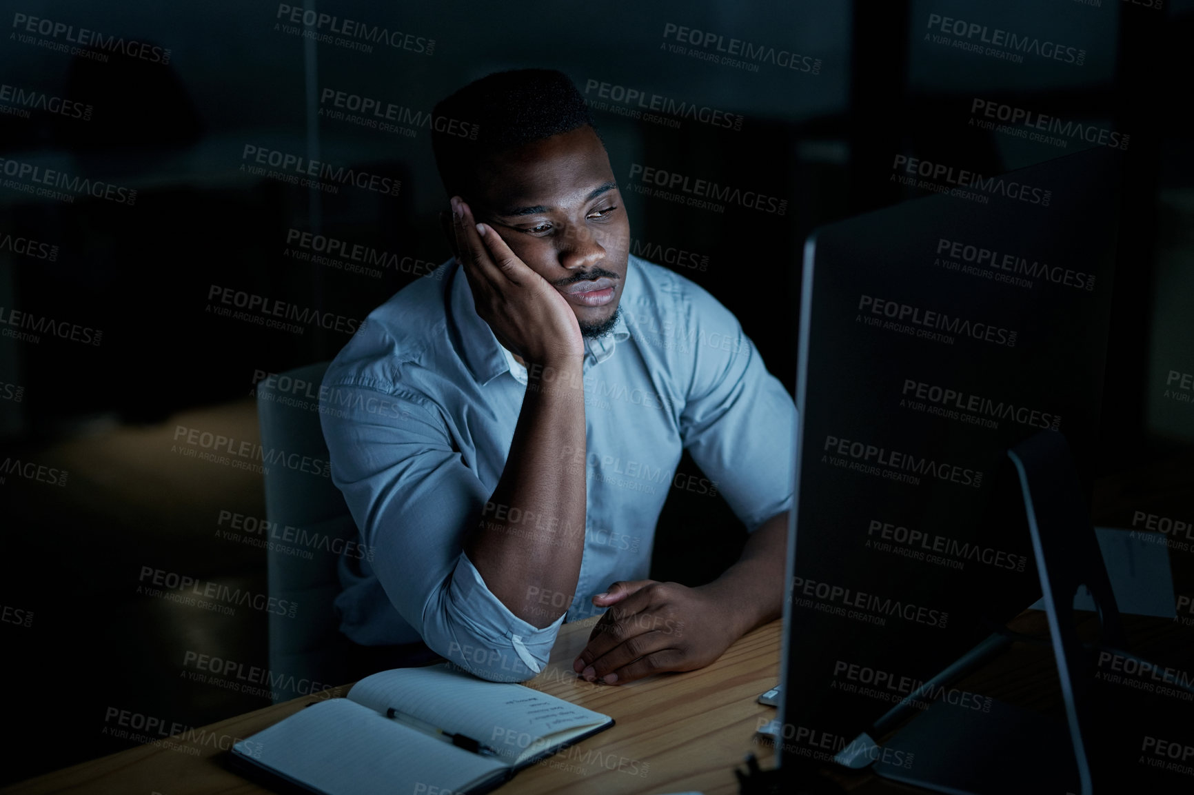 Buy stock photo Shot of a young businessman looking bored while using a computer during a late night at work