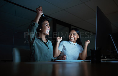 Buy stock photo Shot of two young businesswomen cheering while using a computer during a late night at work