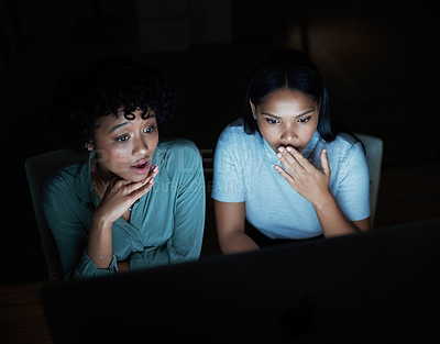 Buy stock photo Shot of two young businesswomen looking shocked while using a computer during a late night at work