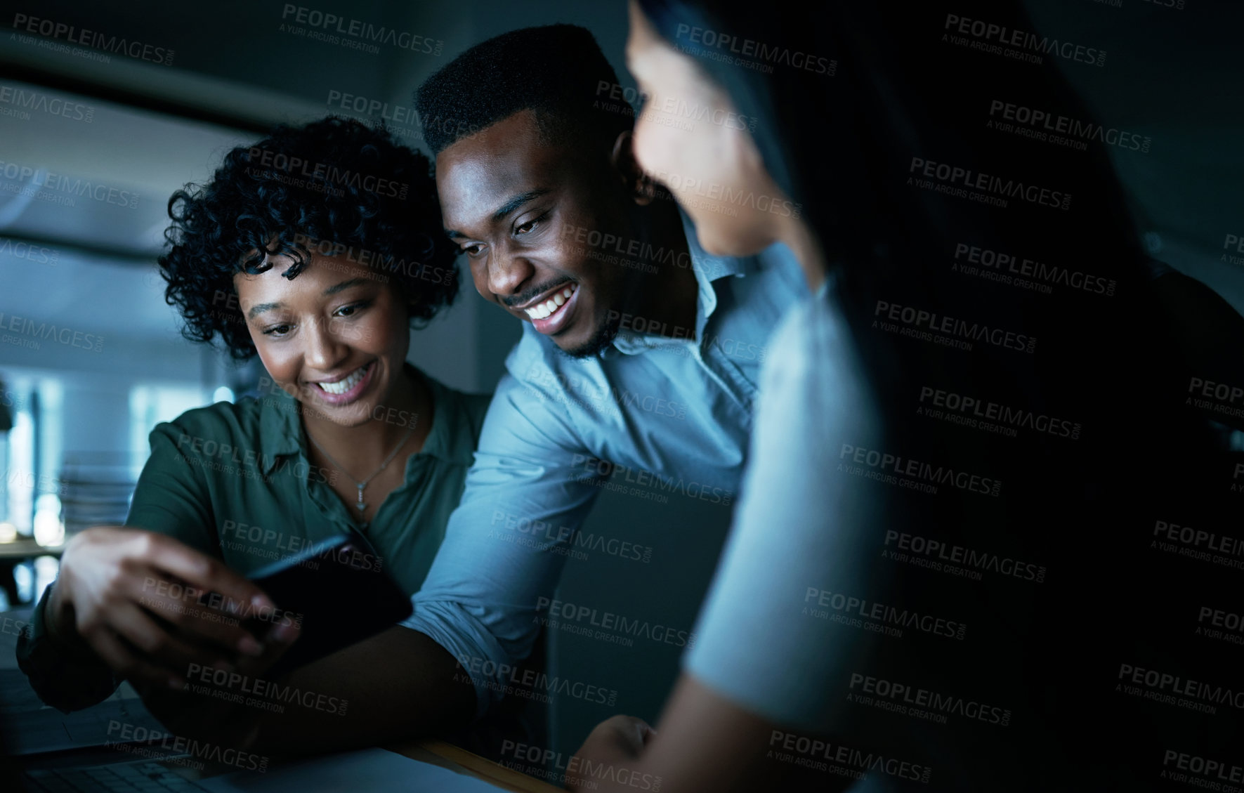 Buy stock photo Shot of a group of young businesspeople using a smartphone together during a late night at work