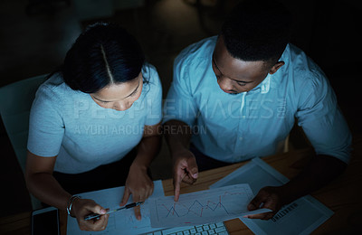 Buy stock photo Shot of a young businesswoman and businessman analysing financial reports during a late night at work