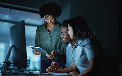 Buy stock photo Shot of a group of young businesspeople using a digital tablet and computer during a late night at work