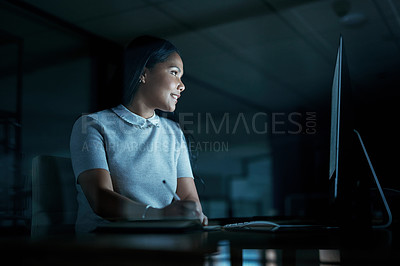 Buy stock photo Shot of a young businesswoman writing in a notebook and using a computer during a late night at work