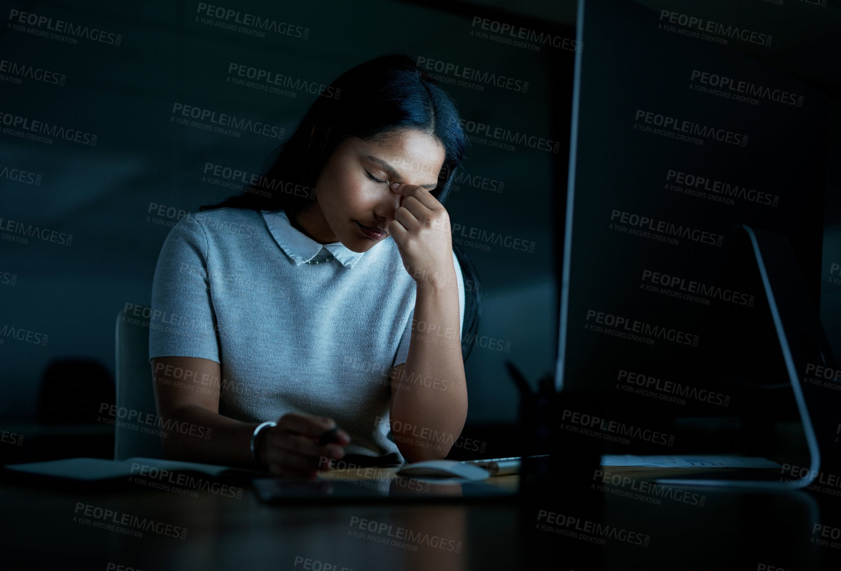 Buy stock photo Shot of a young businesswoman looking stressed while using a computer during a late night at work