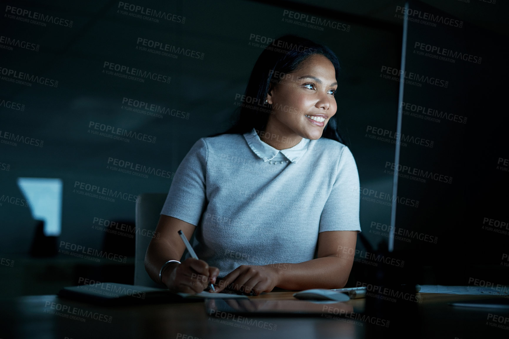 Buy stock photo Shot of a young businesswoman writing in a notebook and using a computer during a late night at work