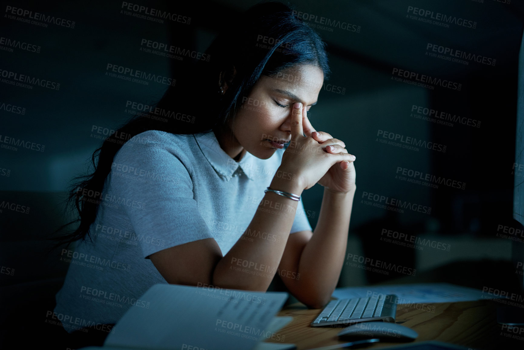 Buy stock photo Shot of a young businesswoman looking stressed while using a computer during a late night at work