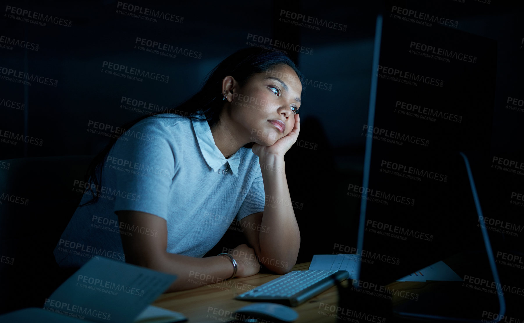 Buy stock photo Shot of a young businesswoman looking bored while using a computer during a late night at work