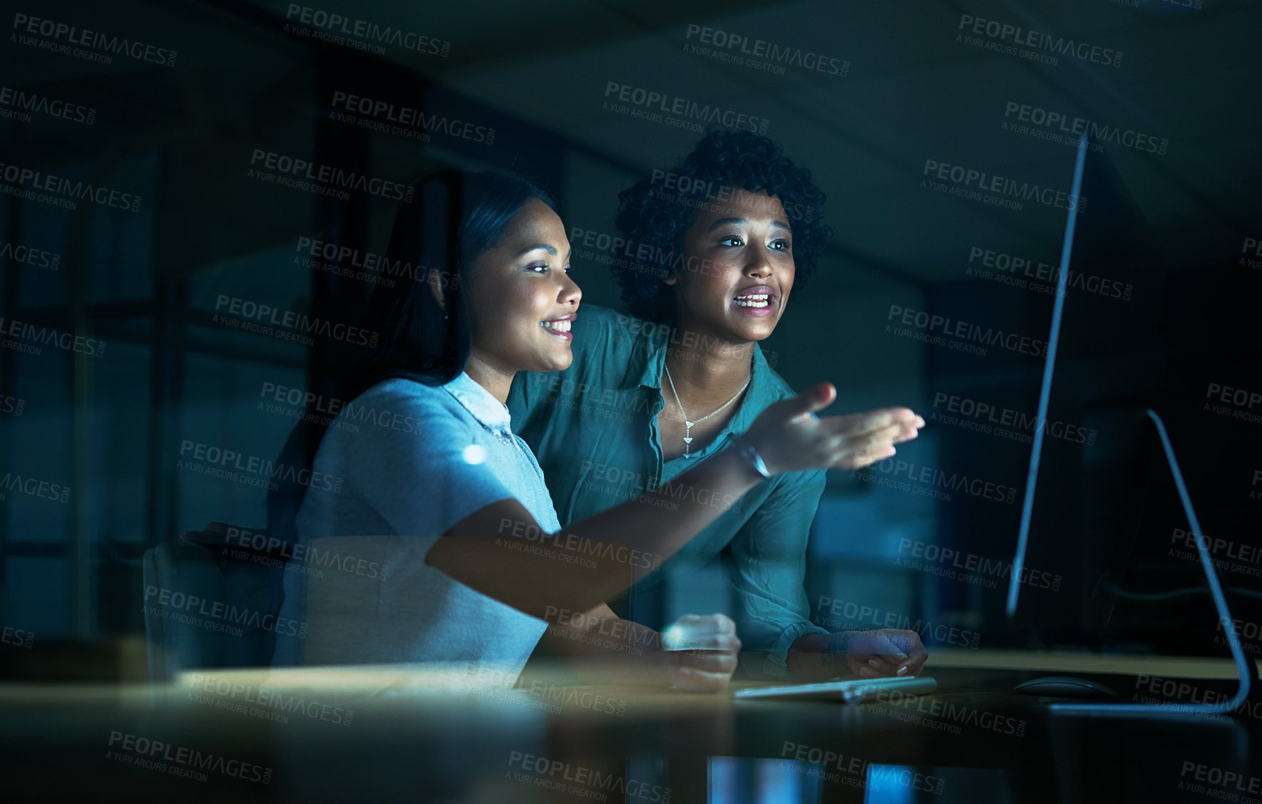 Buy stock photo Shot of two young businesswomen using a computer together during a late night at work