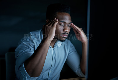 Buy stock photo Shot of a young businessman looking stressed while using a computer during a late night at work