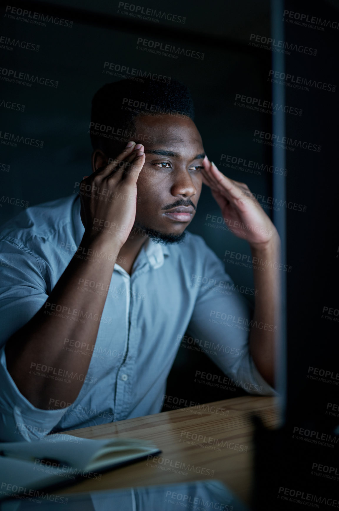 Buy stock photo Shot of a young businessman looking stressed while using a computer during a late night at work