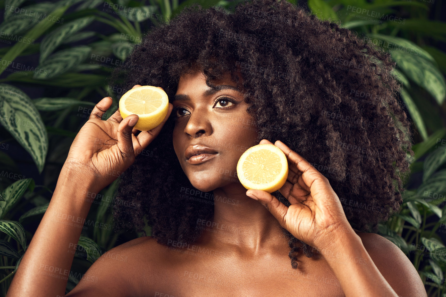 Buy stock photo Shot of a beautiful young woman holding juicy lemon halves against a leafy background