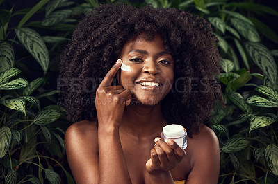 Buy stock photo Shot of a beautiful young woman applying moisturiser to her face against a leafy background