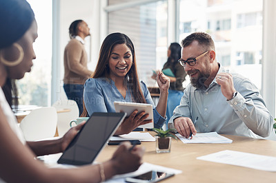 Buy stock photo Cropped shot of two business coworkers sitting together and celebrating an achievement together while their colleagues work around them