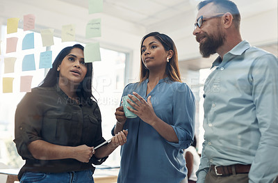 Buy stock photo Cropped shot of a diverse group of businesspeople standing together and using a glass board to brainstorm in the office