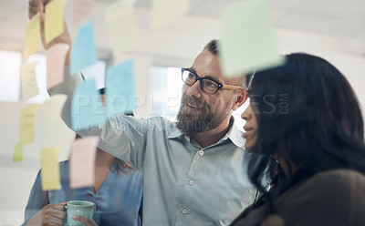 Buy stock photo Cropped shot of a diverse group of businesspeople standing together and using a glass board to brainstorm in the office