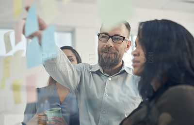 Buy stock photo Cropped shot of a diverse group of businesspeople standing together and using a glass board to brainstorm in the office